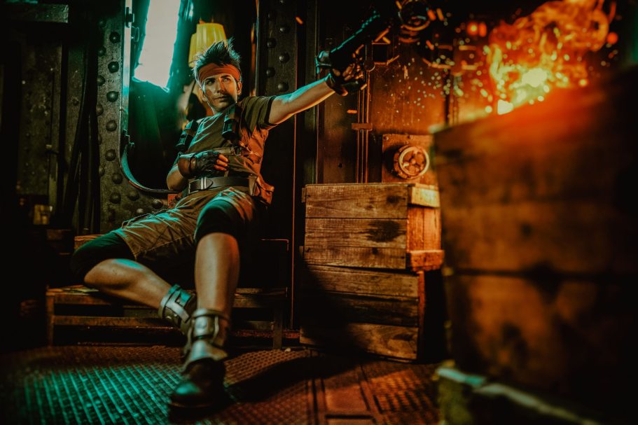Eine Person in einer grünlich beleuchteten Umgebung zielt mit einer Waffe auf ein Feuer.